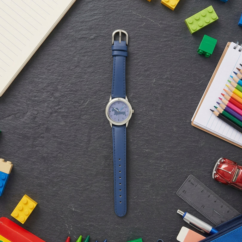 A wristwatch with a blue strap and a silver-toned round case, laid flat on a dark slate surface with colorful toy blocks, pencils, and keys around it.