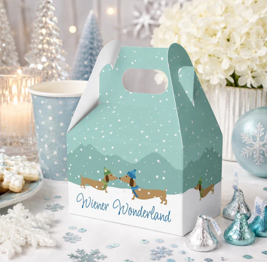 A winter-themed dachshund party favor box with a mint green and white design, decorated with dachshunds in snow boots under falling snow, and the text 'Wiener Wonderland'. The box is styled on a table with holiday treats, a paper cup, and festive decorations.